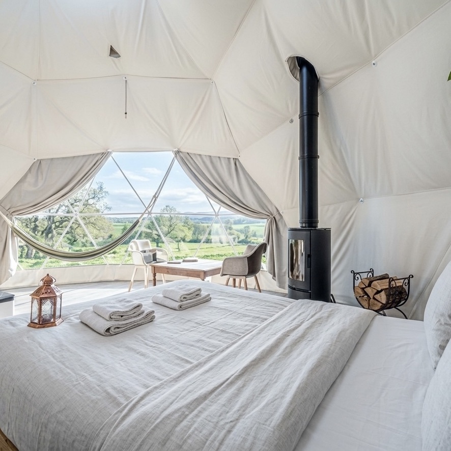 Intérieur d'un dôme avec poêle à bois, lit douillet et vue sur la campagne